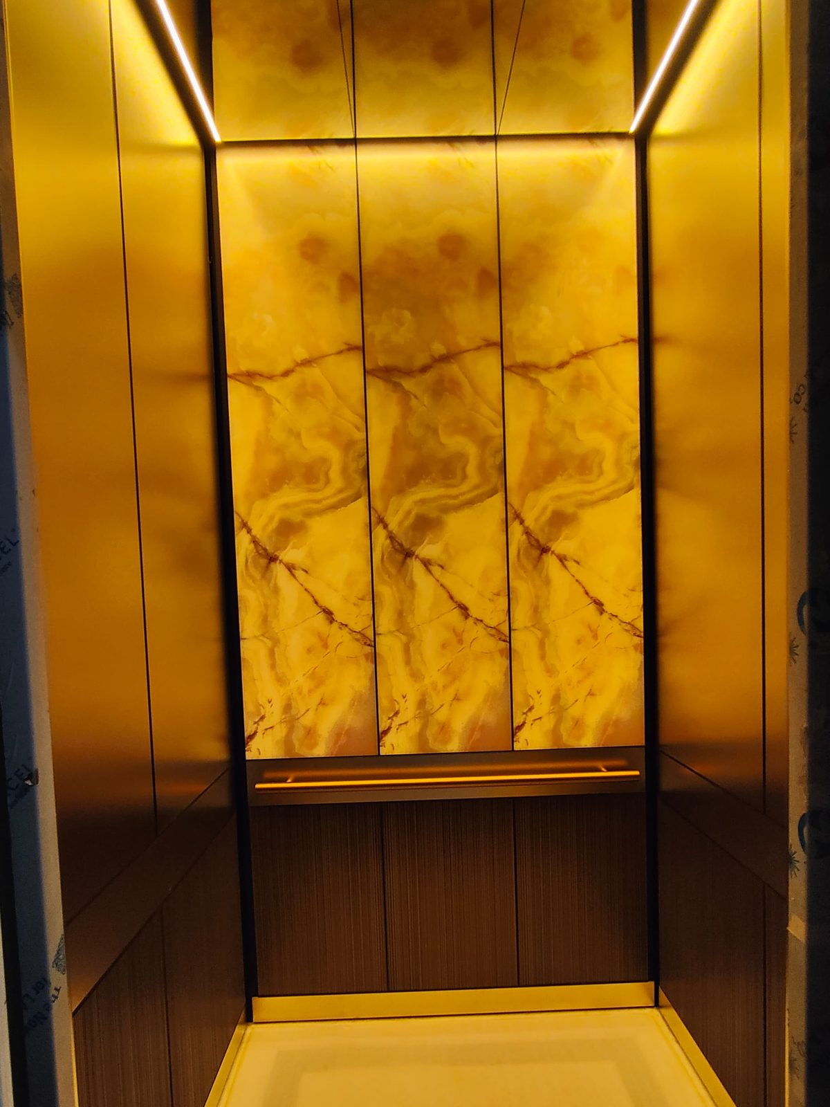 Lift cabin finished in brass with a backlit onyx rear panel
